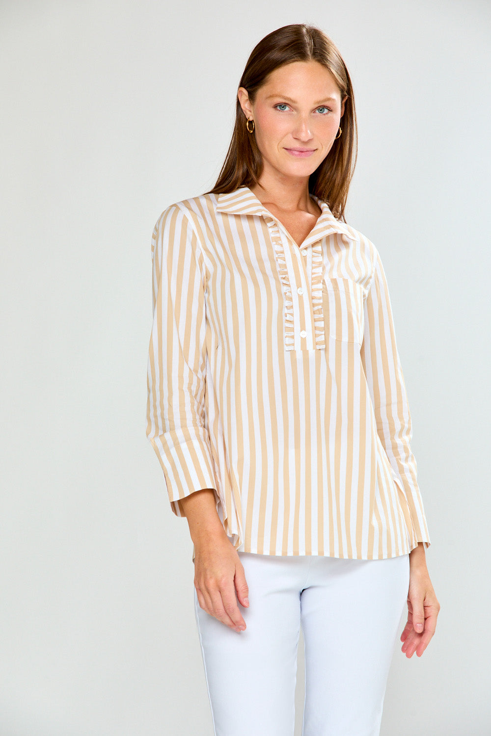 Woman wearing a striped blouse and white pants against a plain background