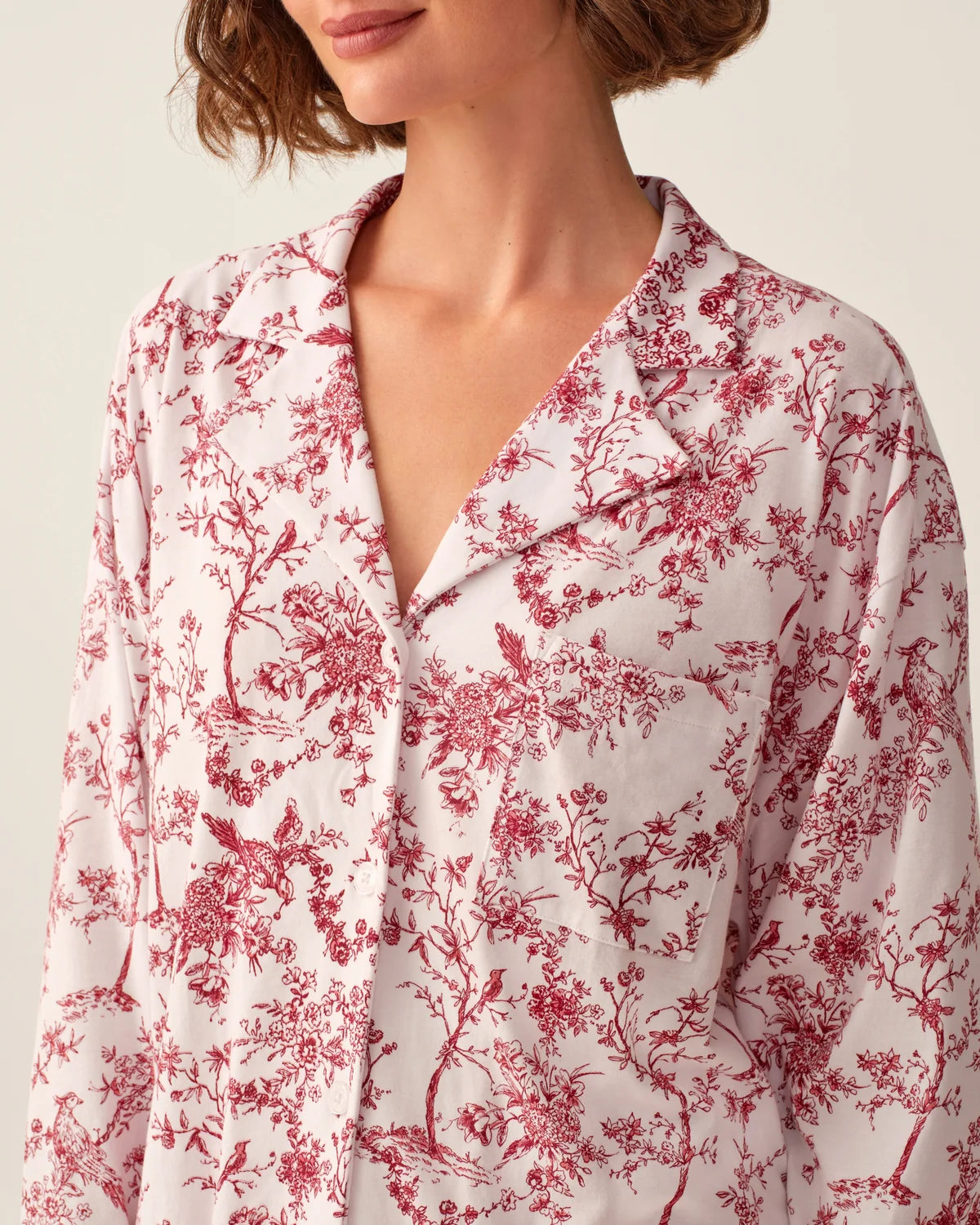A close-up of a model wearing a long-sleeve collared button-front shirt with a red toile-style floral and bird pattern on a white background.