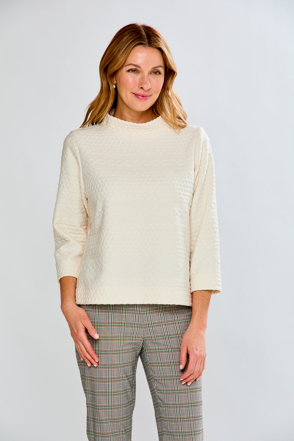 Woman wearing a cream sweater and plaid pants against a white background
