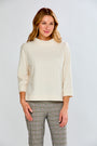 Woman wearing a cream sweater and plaid pants against a white background