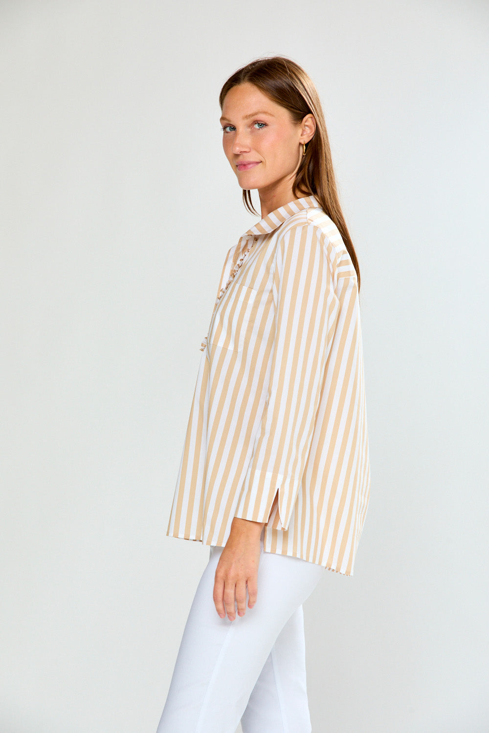Woman wearing a striped shirt and white pants against a plain background