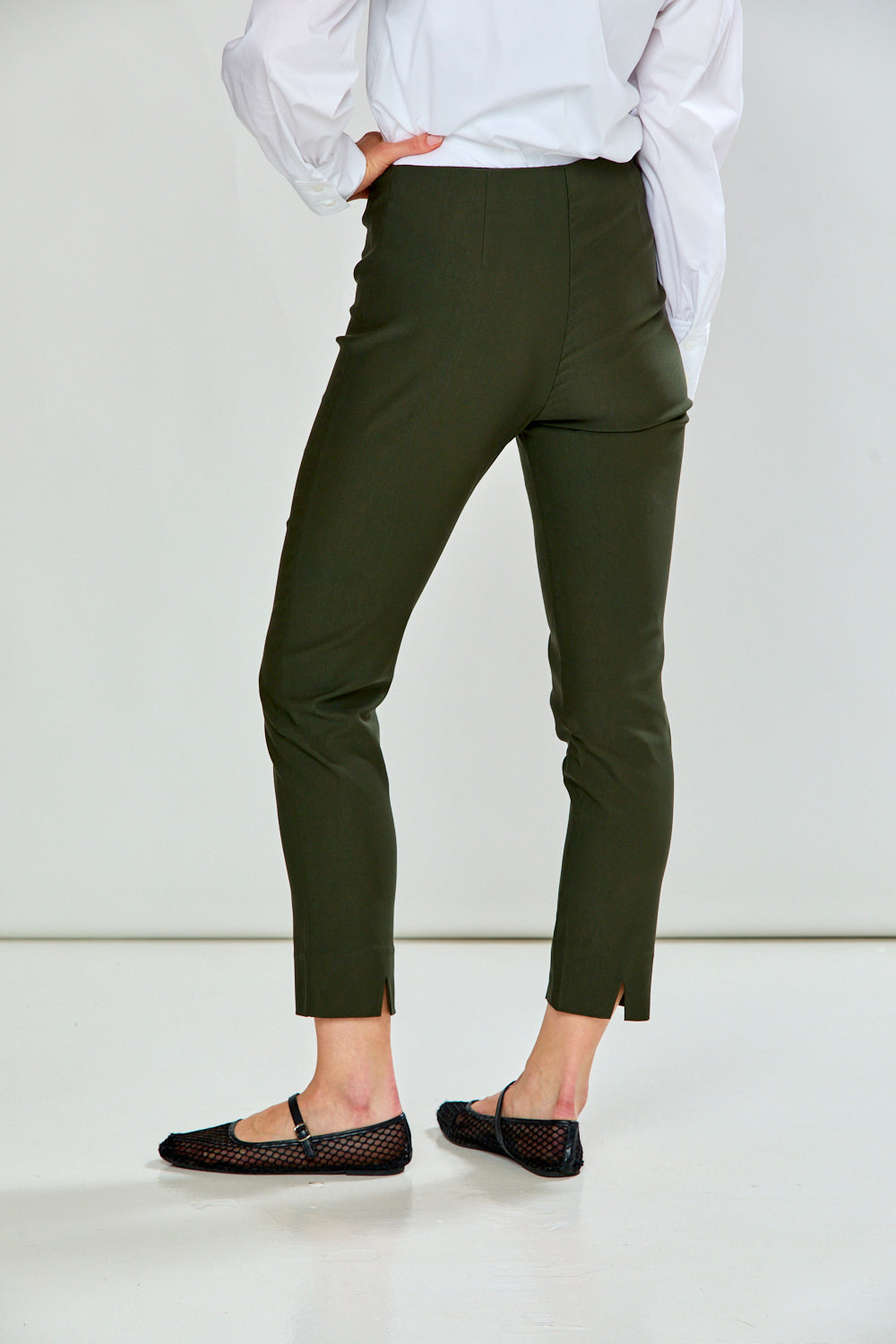 A model wearing green cropped trousers, styled with a white long-sleeve button-up shirt and black flat shoes, shown from the waist down against a plain white studio background.