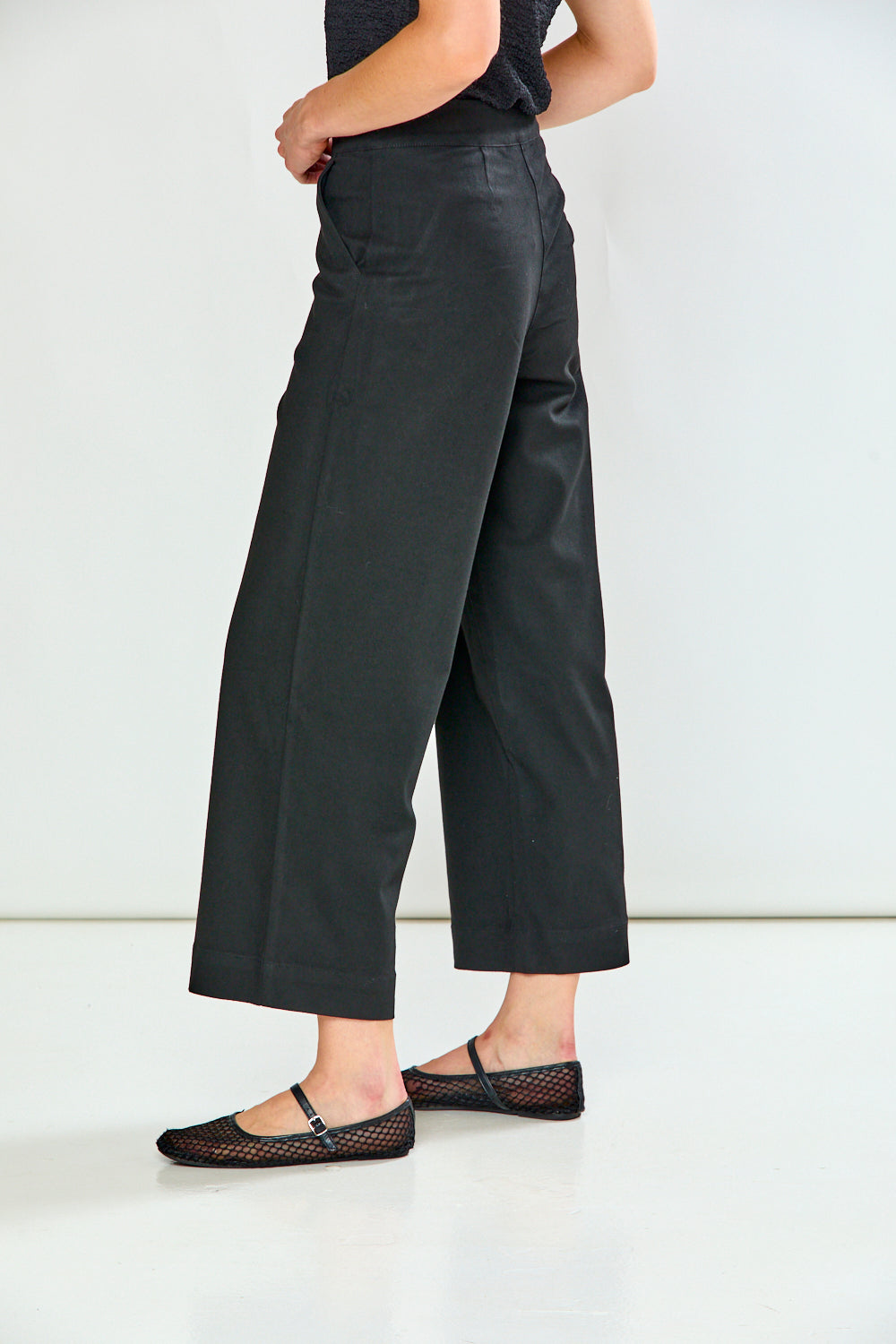A person shown from the waist down wearing black wide-leg cropped pants and black flat shoes against a plain white studio background.