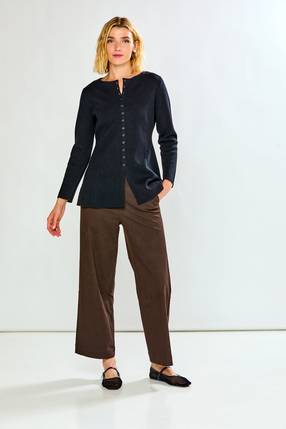 A woman modeling a dark navy long-sleeve button-front top with brown wide-leg cropped pants and black flats, standing against a plain white studio background.