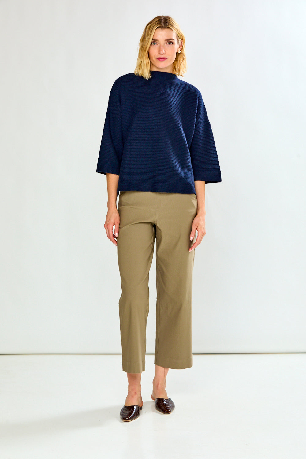 A model wearing a pair of mushroom cropped wide-leg trousers, paired with a white top and dark brown flat shoes, against a plain white studio background.