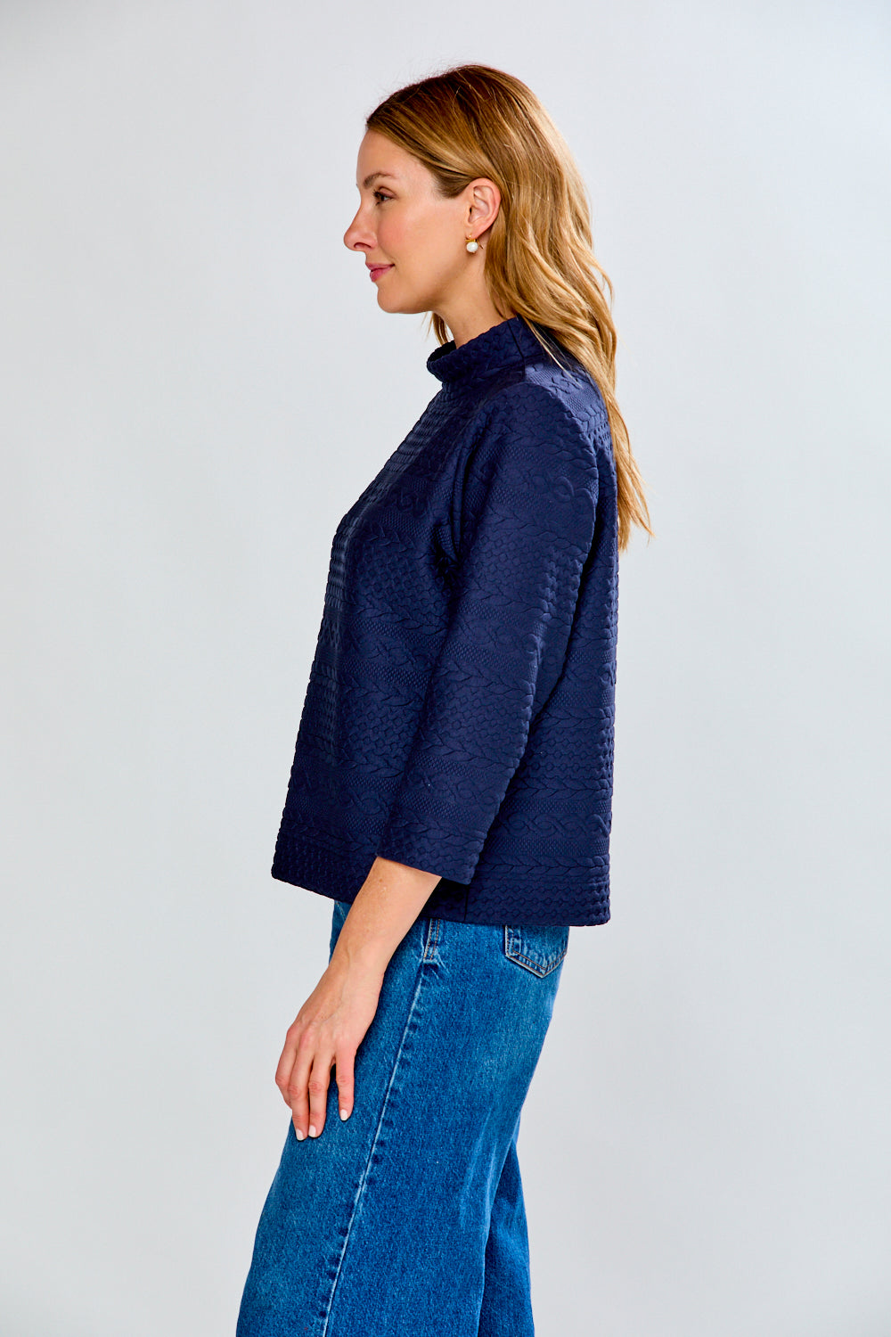 Woman wearing a navy blue textured sweater and blue jeans on a white background