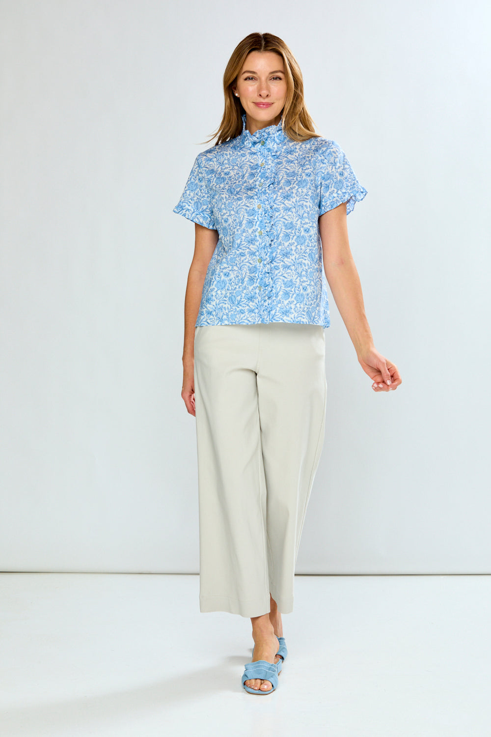 Woman wearing a blue floral blouse and white pants on a white background