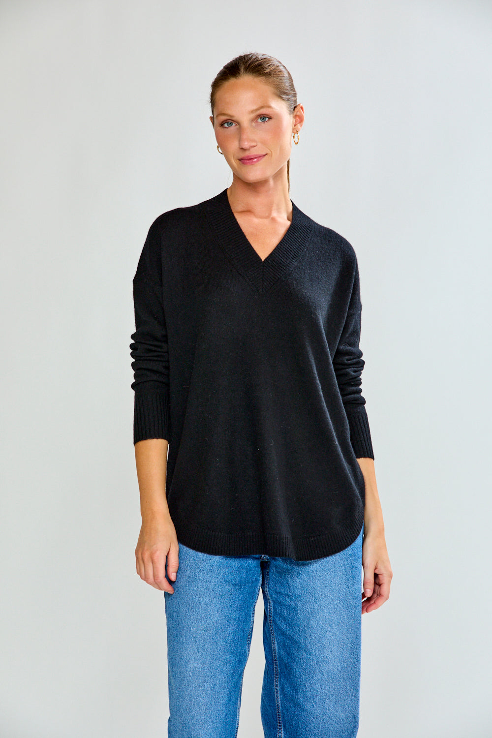 Woman wearing a black sweater and blue jeans against a plain background
