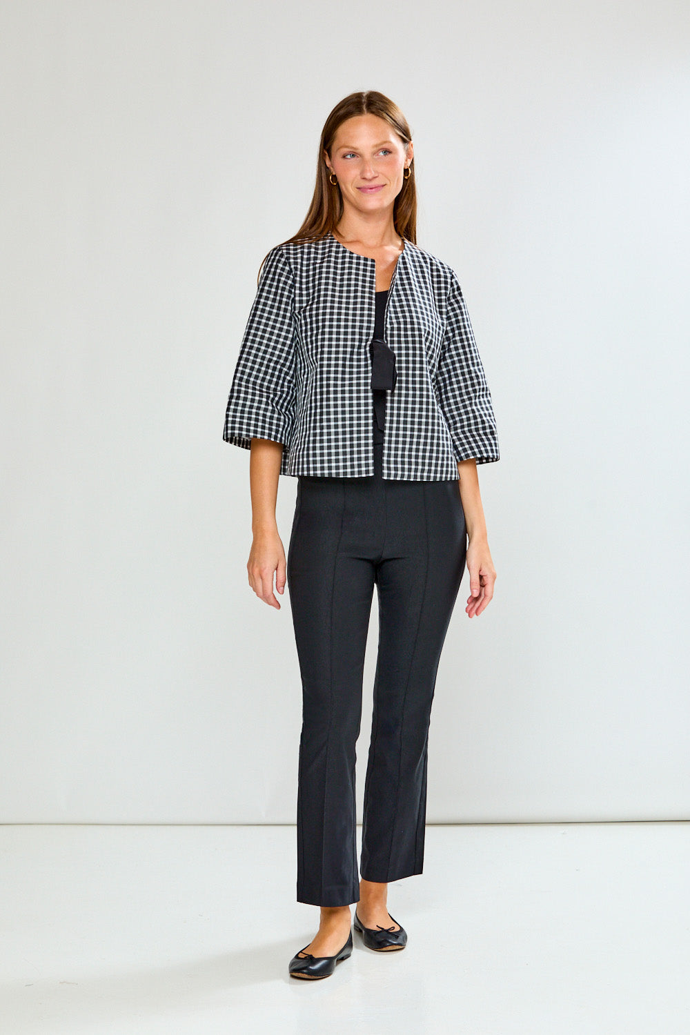 Woman wearing a black and white checkered jacket and black pants on a white background