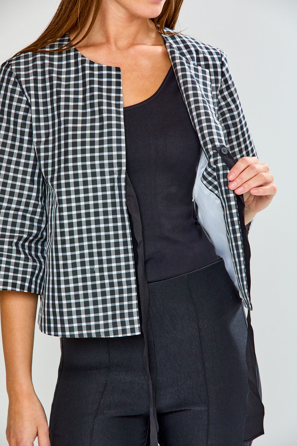 Person wearing a black and white checkered jacket over a black top and pants on a light gray background