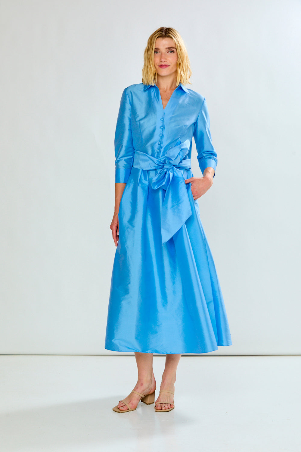 The Ainsley Dress - Light Blue shown as a chic womens dress with a collared neckline long sleeves button front tie waist and flowing midi skirt