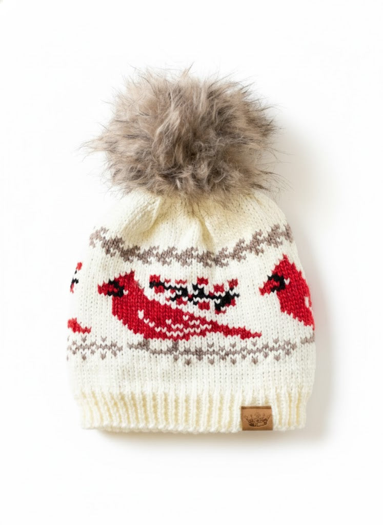 Knitted hat with red bird design and fur pom-pom on a white background