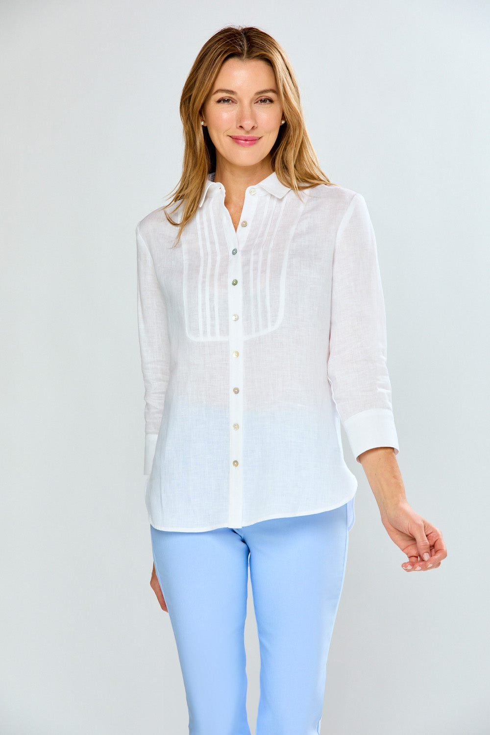 Woman wearing a white blouse and light blue pants on a plain background