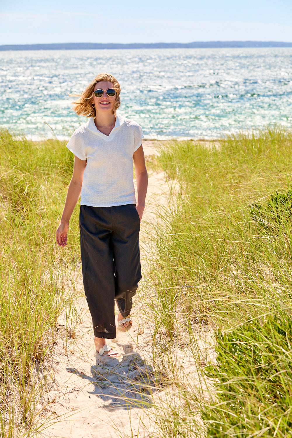 Woman walking on a sandy path near the ocean with sunglasses on