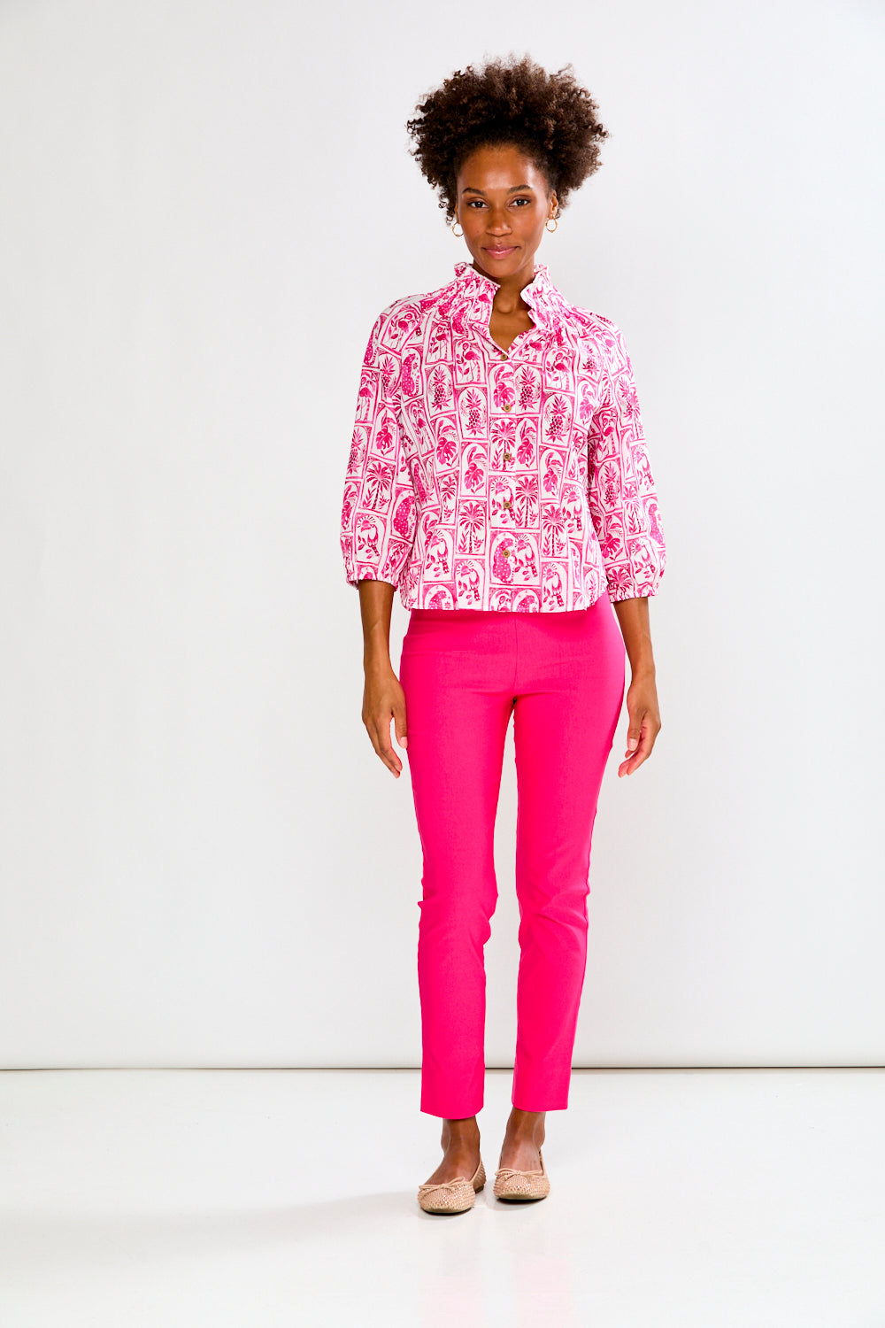 Woman wearing a pink patterned blouse and pink pants on a white background