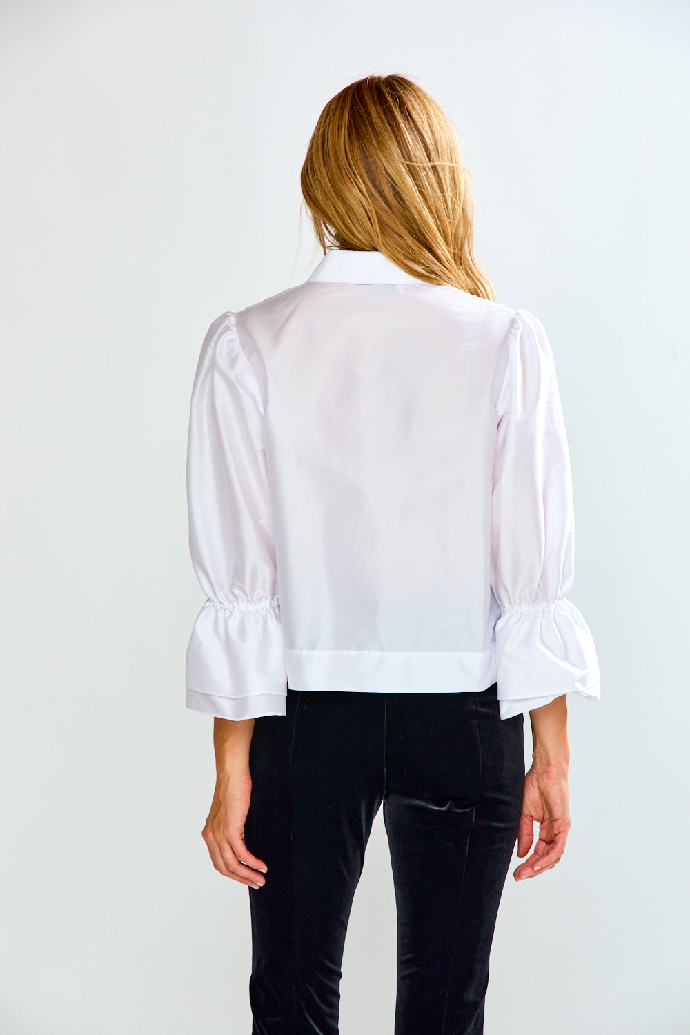 The Arlo Top in Taffeta - White shown from the back with a high collar, puff sleeves, gathered cuffs, and a polished silhouette styled with black pants