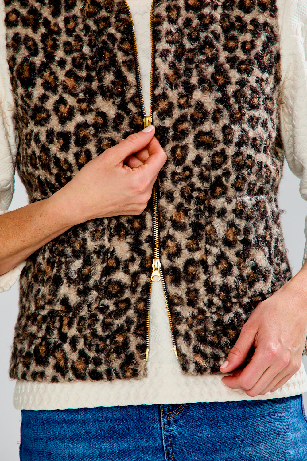 Leopard print vest with a gold zipper being unzipped, worn over a white shirt and blue jeans.