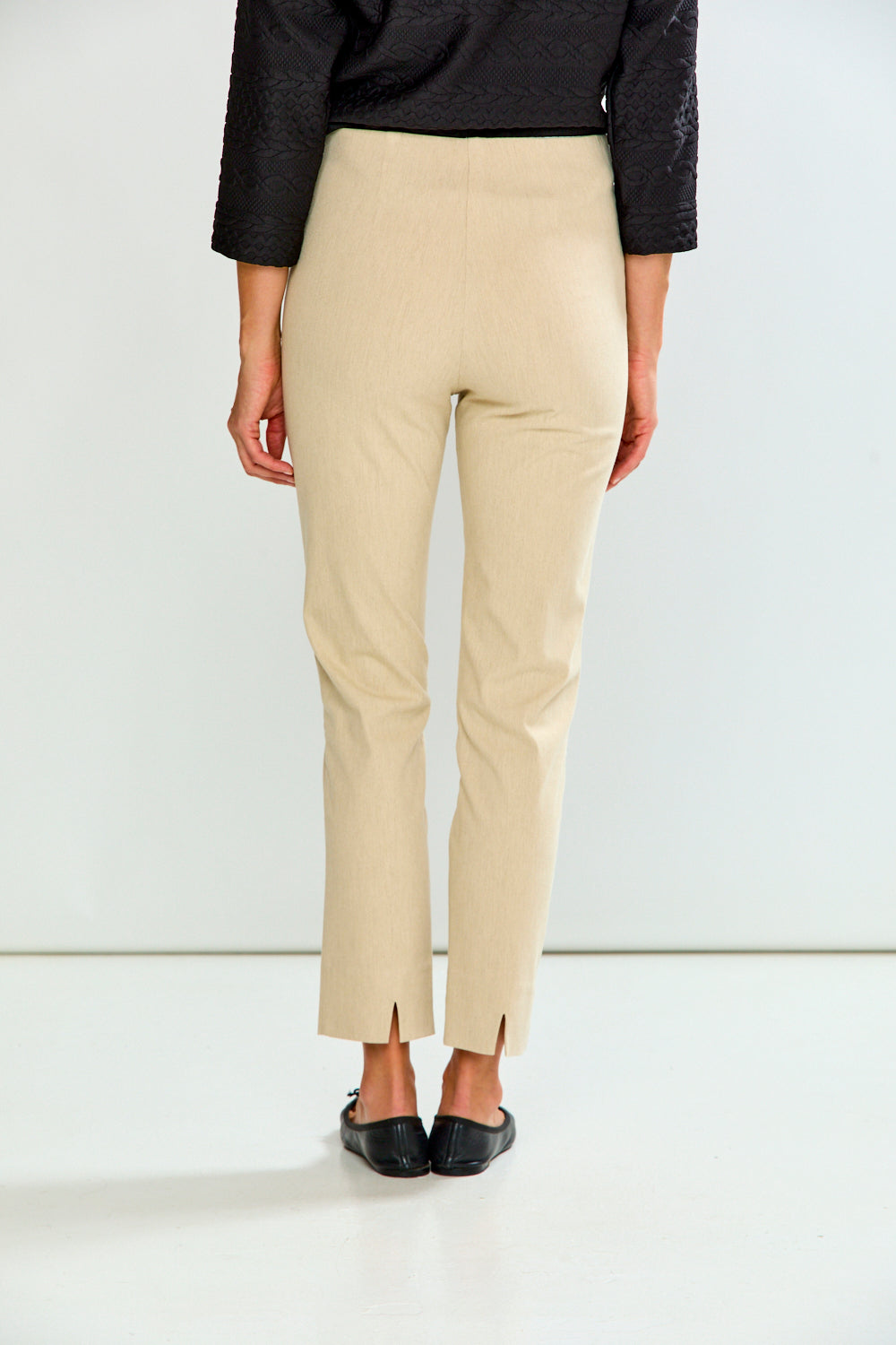A model wearing sand cropped trousers, a black long-sleeve top, and black flat shoes, standing against a plain white studio background.