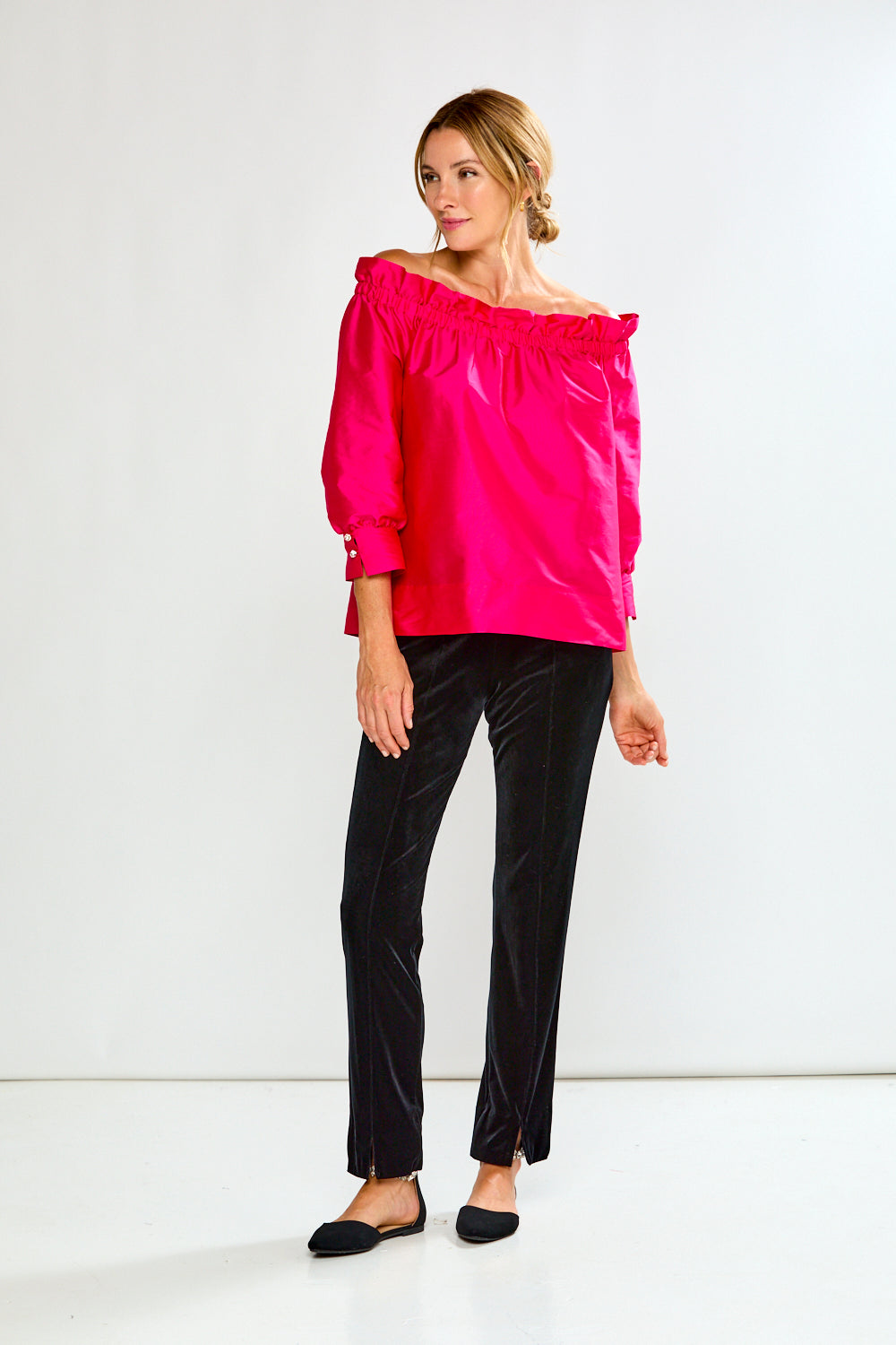 Woman wearing a bright pink off-shoulder top against a white background