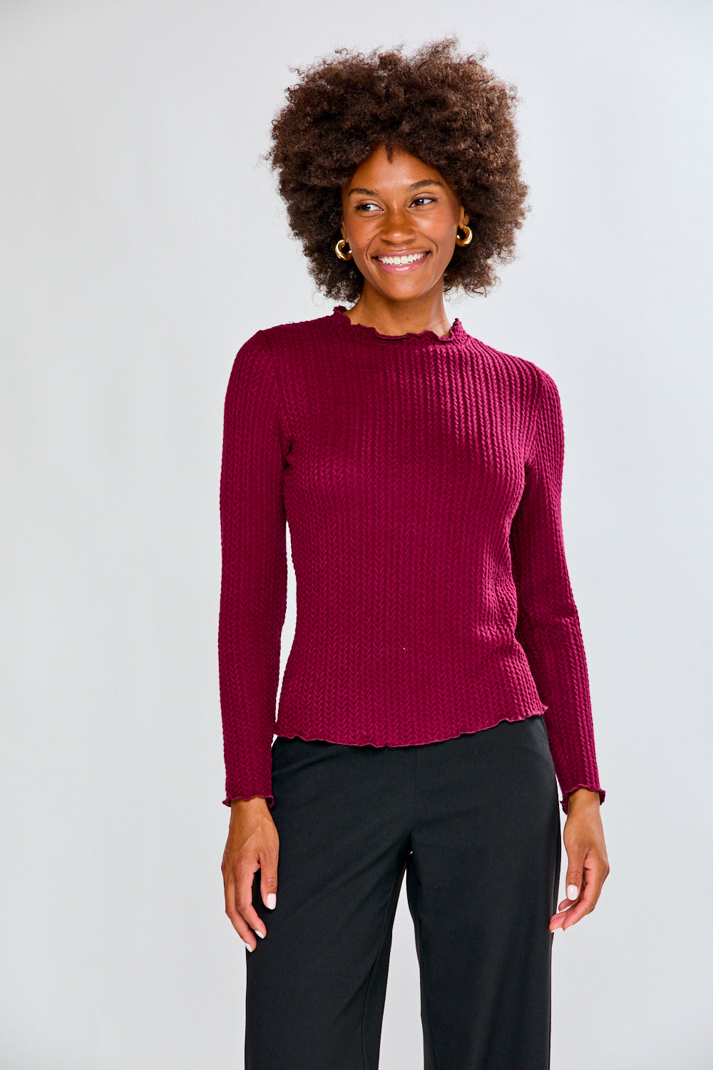Woman wearing a burgundy shirt and black pants against a white background