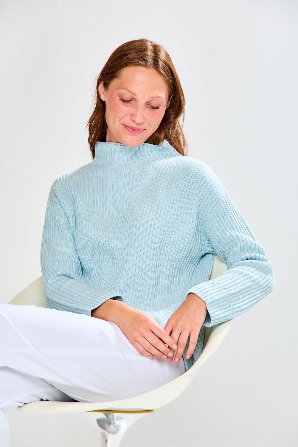 Woman wearing a light blue ribbed sweater and white pants on a plain background
