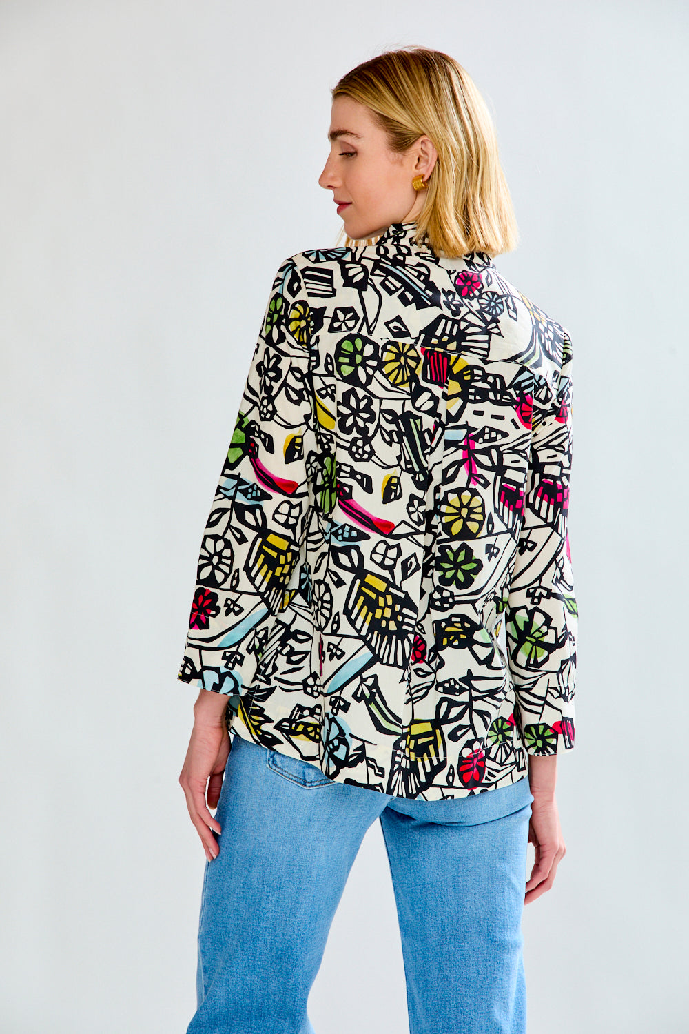 Woman wearing a colorful patterned shirt and blue jeans on a white background