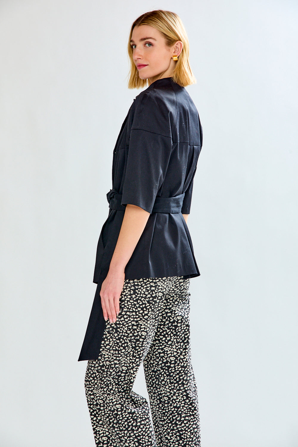 Woman wearing a black belted jacket and patterned pants on a white background