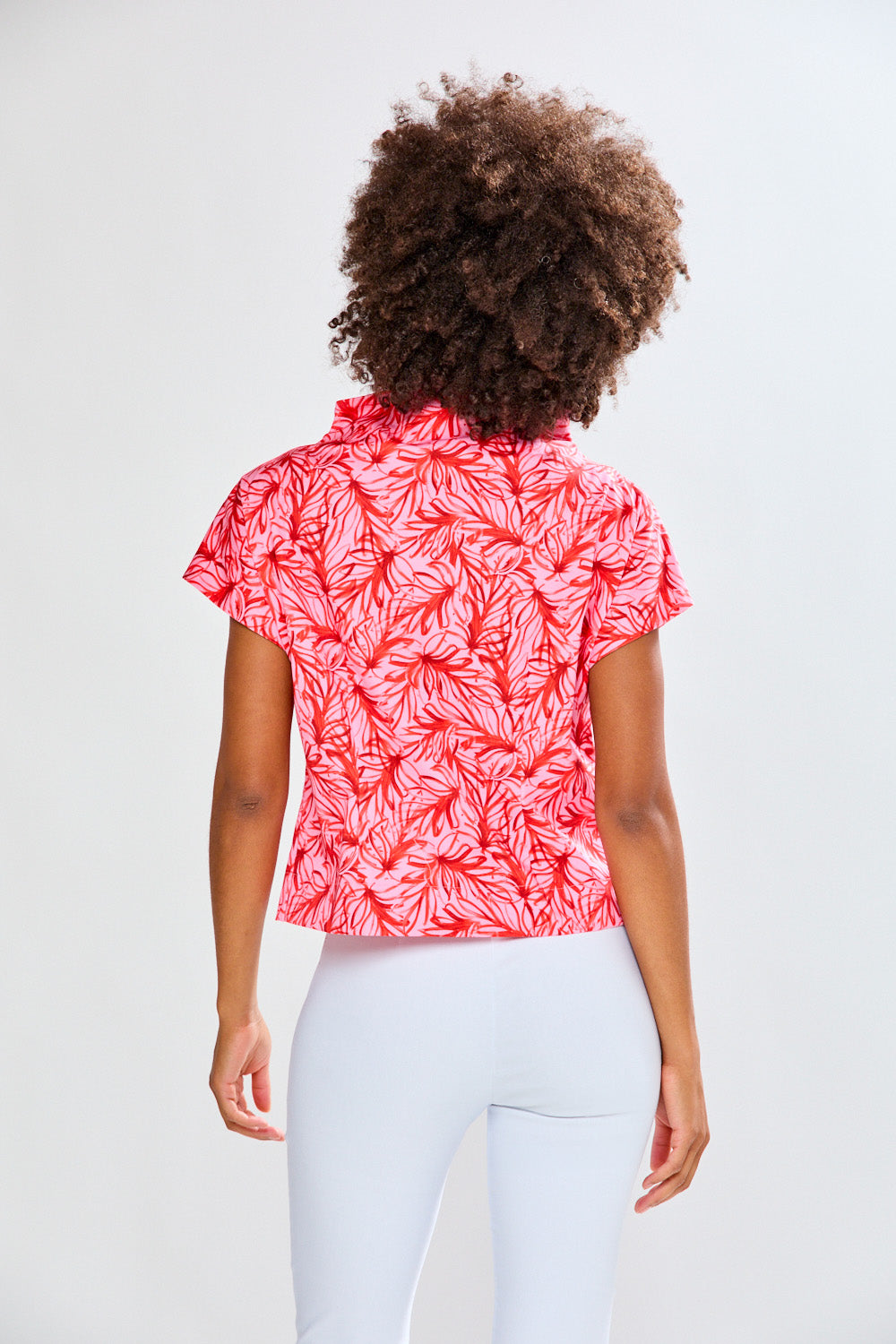 Person wearing a red leaf patterned shirt and white pants on a light gray background