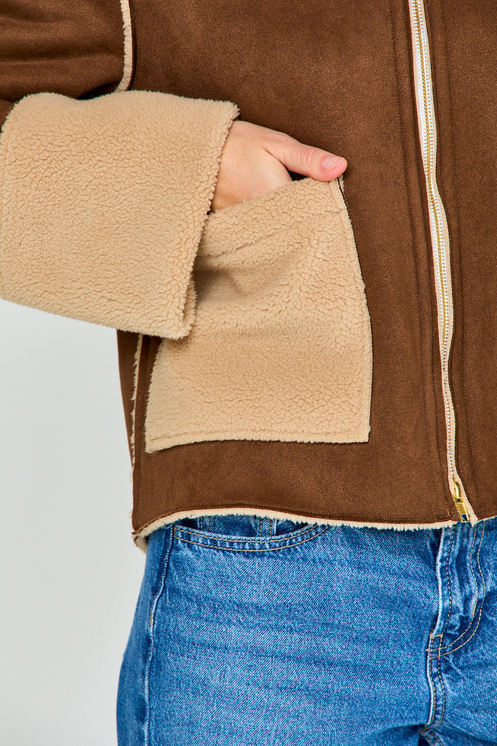 Woman wearing a brown and beige jacket with blue jeans on a white background