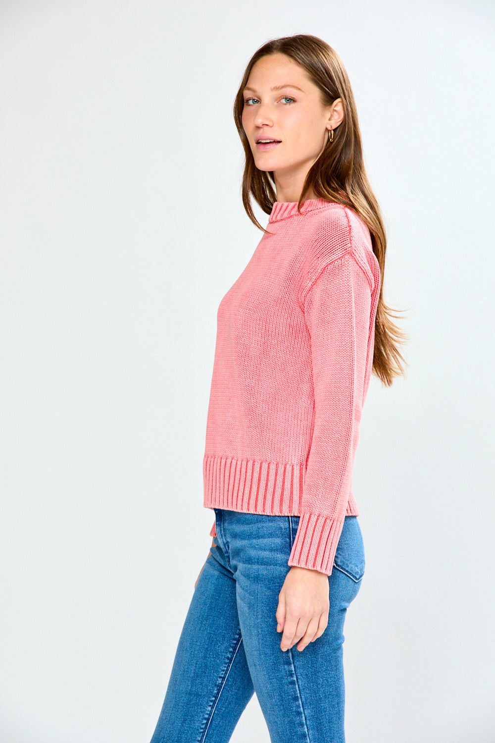 Woman wearing a guava sweater and blue jeans on a white background