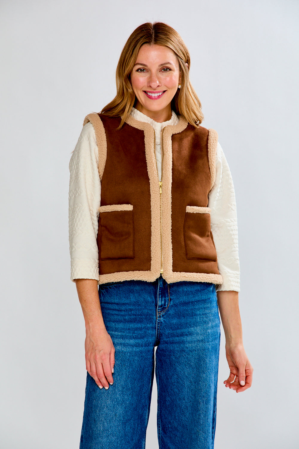 Woman wearing a brown and beige vest with blue jeans on a white background
