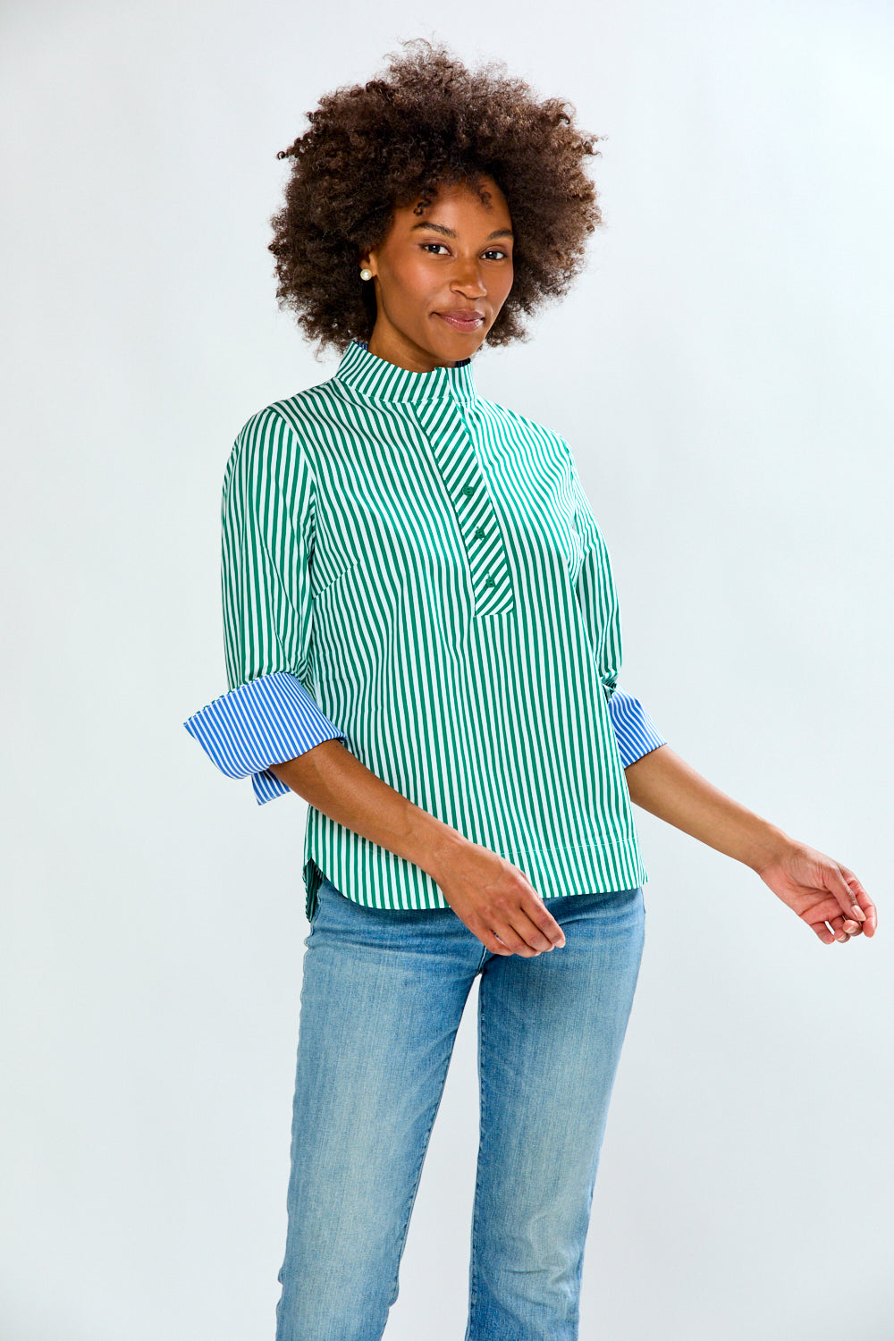 Woman wearing a green and white striped shirt with rolled-up sleeves and blue jeans on a light gray background
