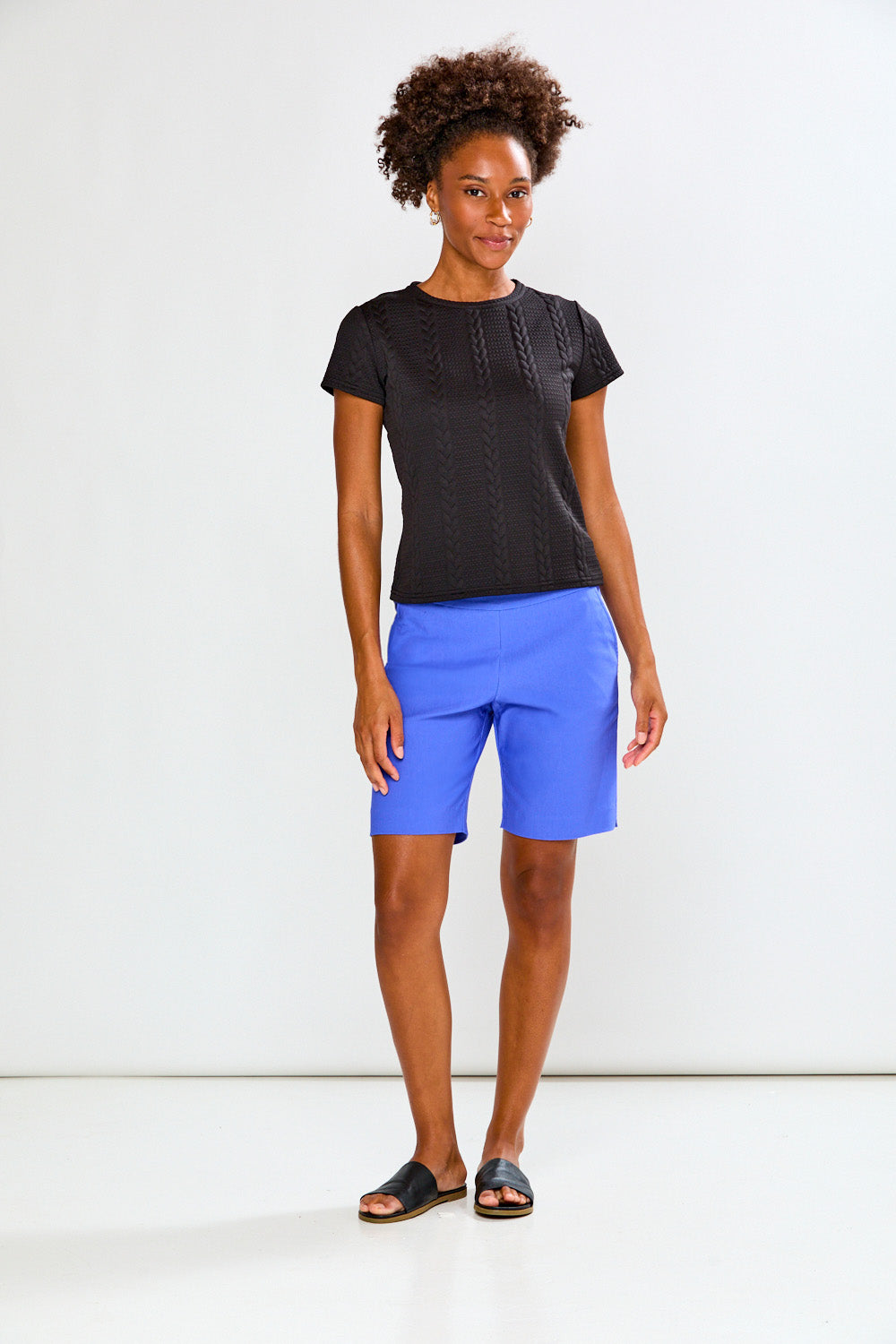 Woman wearing a black textured top and blue pants on a white background