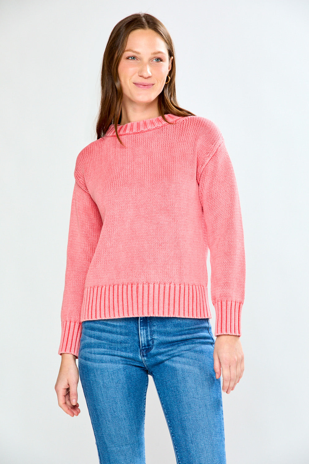 Woman wearing a guava sweater and blue jeans on a white background