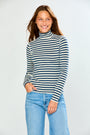 A woman wearing a navy and cream horizontal striped turtleneck sweater and light blue jeans, standing against a light gray studio background.
