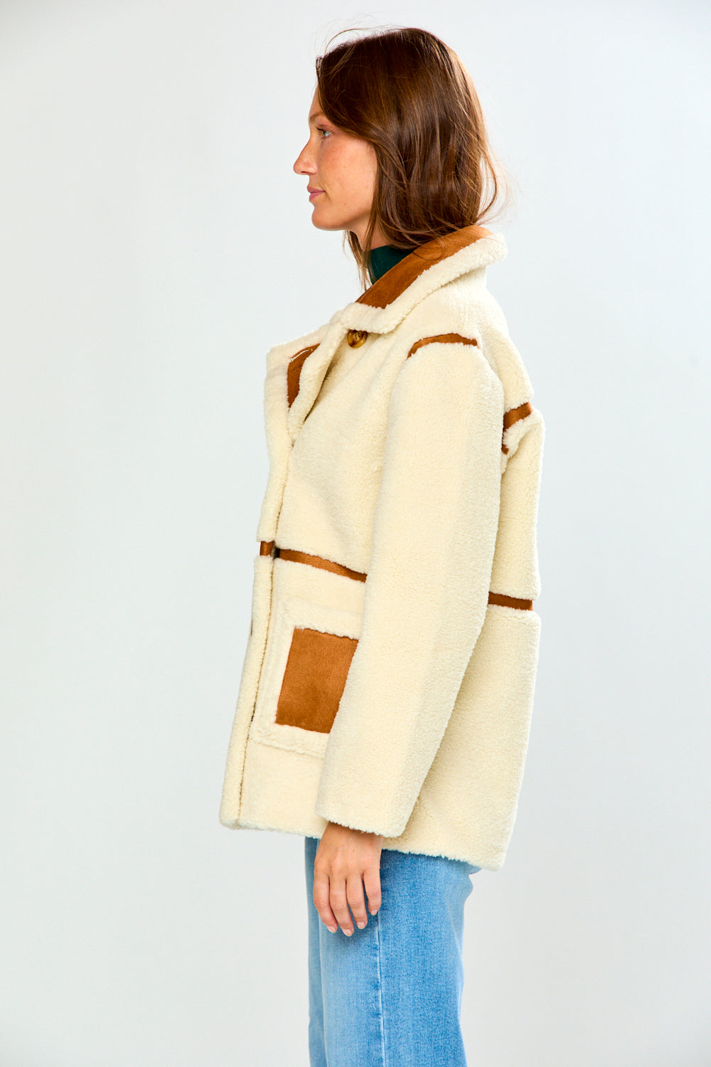 The Phoenix Coat - Tan worn by a woman in profile featuring a cream shearling finish brown trim and patch pockets with blue jeans