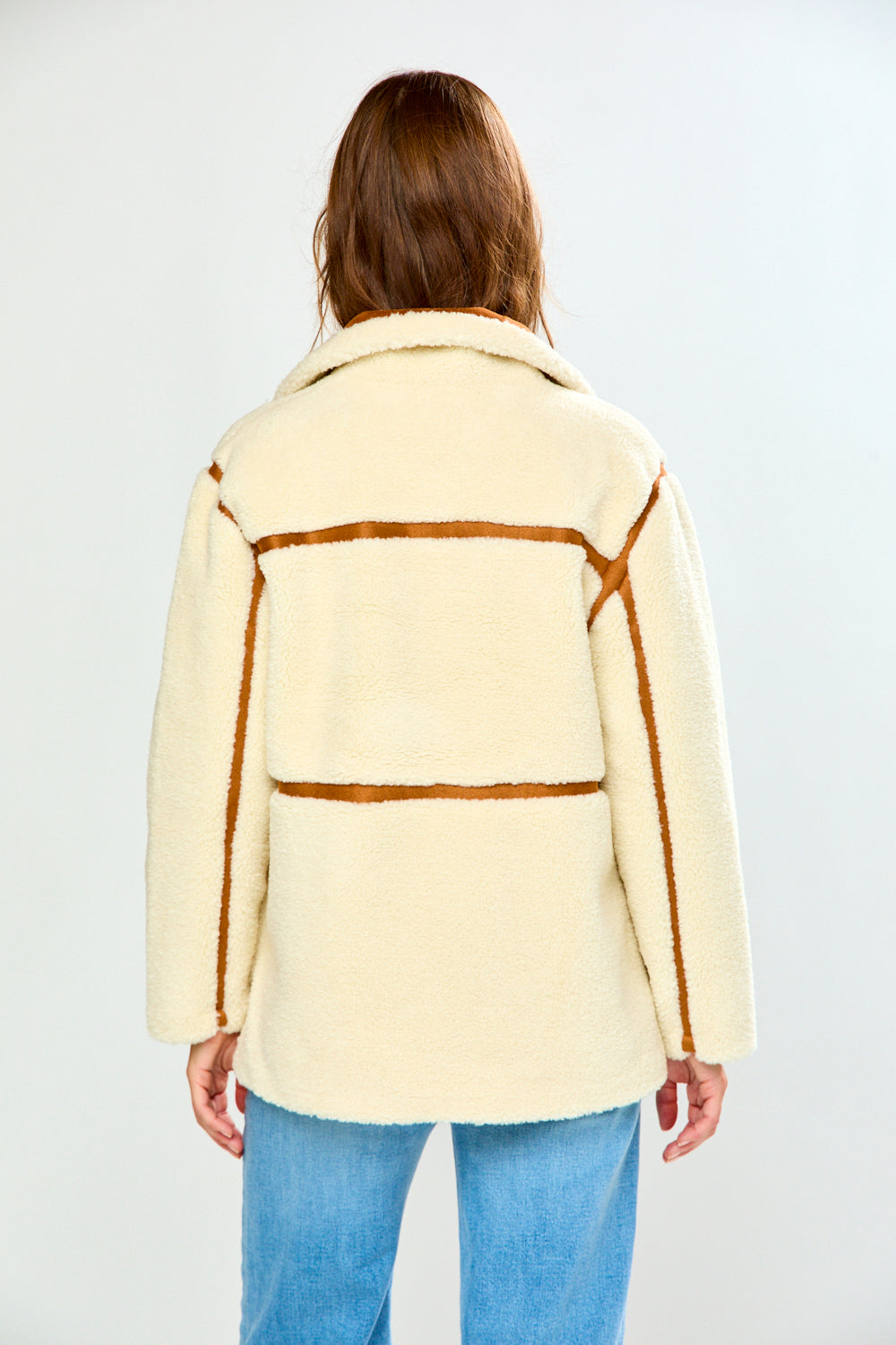 The Phoenix Coat - Tan viewed from the back on a woman in a cream textured jacket with brown trim and blue jeans for a sophisticated timeless look