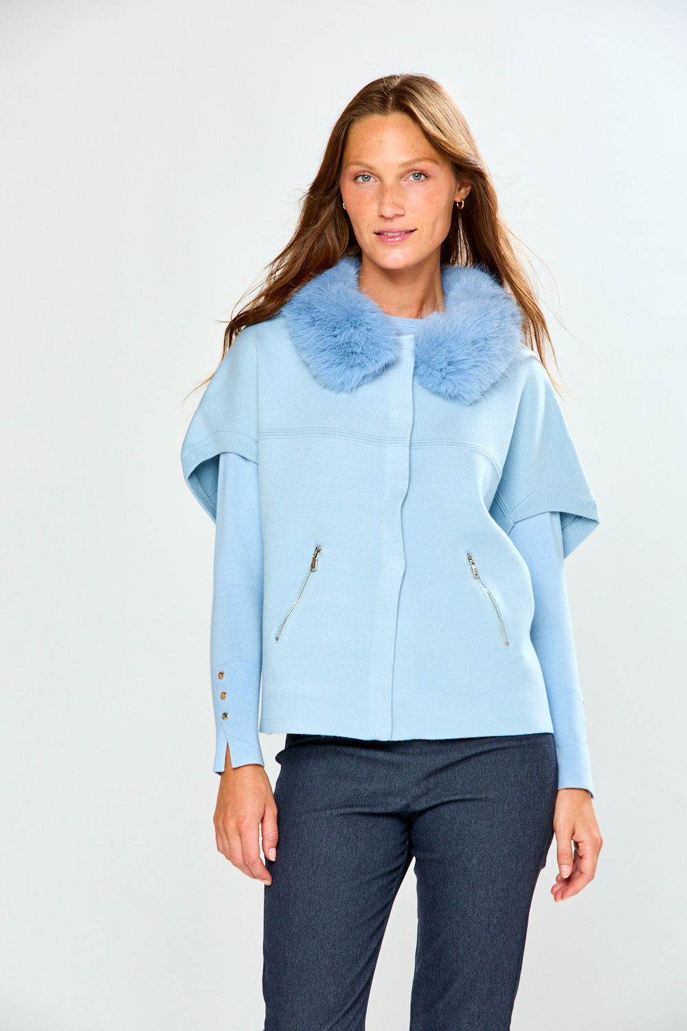 A woman modeling a light blue cropped sweater with a fluffy light blue faux-fur collar, paired with dark gray trousers, against a plain light gray studio background.