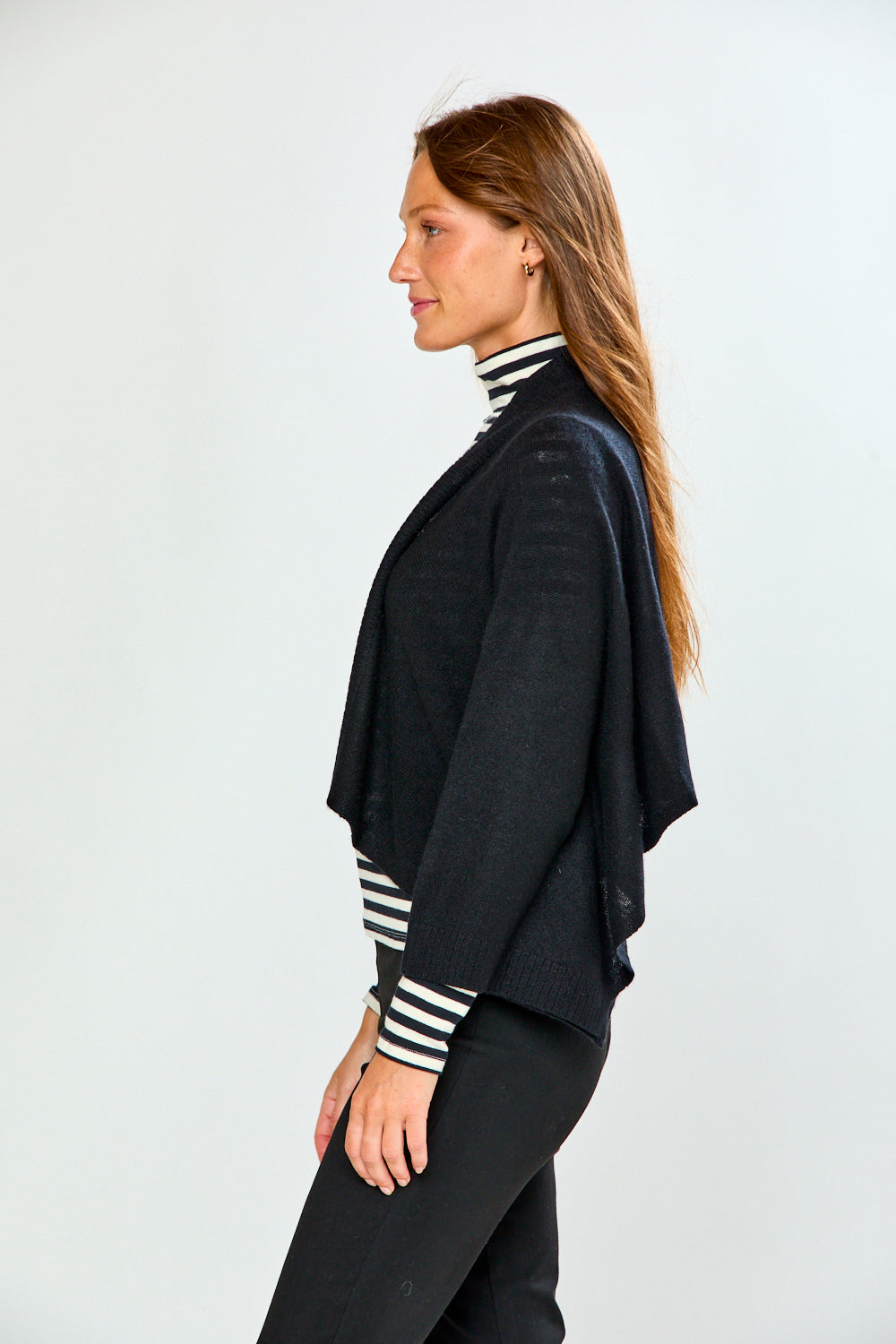 The Shrug with Kimono Sleeves in Black shown in profile on a model over a striped turtleneck with black pants for a chic sophisticated look