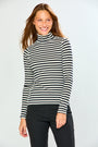 A woman wearing a black and white horizontally striped long-sleeve turtleneck sweater, paired with black pants, standing against a light gray studio background.