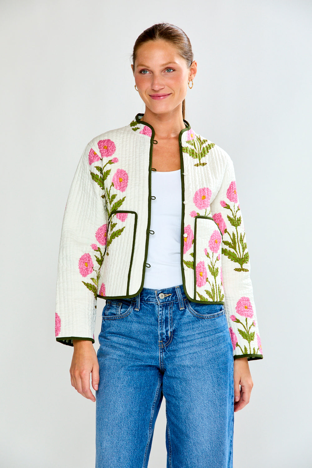 Woman wearing a floral embroidered jacket and blue jeans on a white background