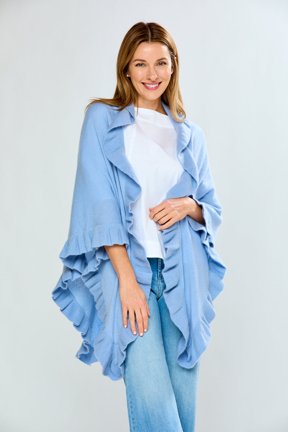 Woman wearing a light blue ruffled jacket over a white top and jeans on a white background