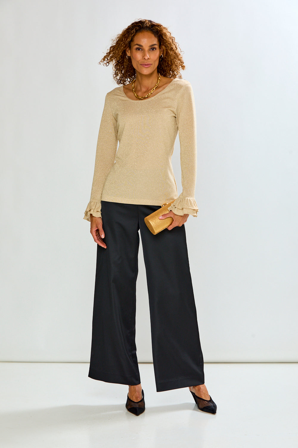 The Jonie Top - Gold shown on a woman with long sleeves and ruffled cuffs styled with black wide leg pants for a sophisticated look