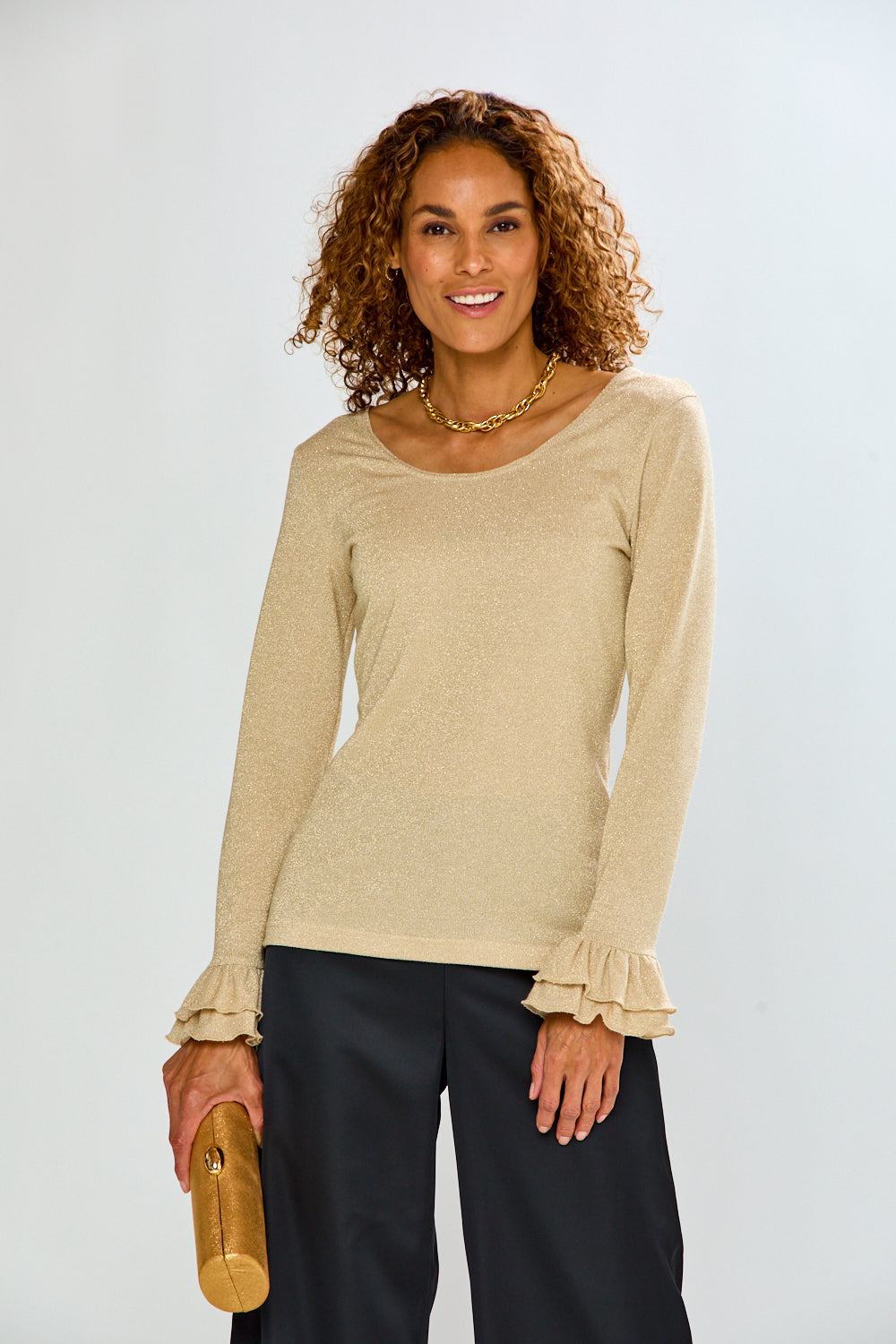 The Jonie Top - Gold, a sophisticated women's knit top with long sleeves and ruffled cuffs, styled with black pants on a smiling model