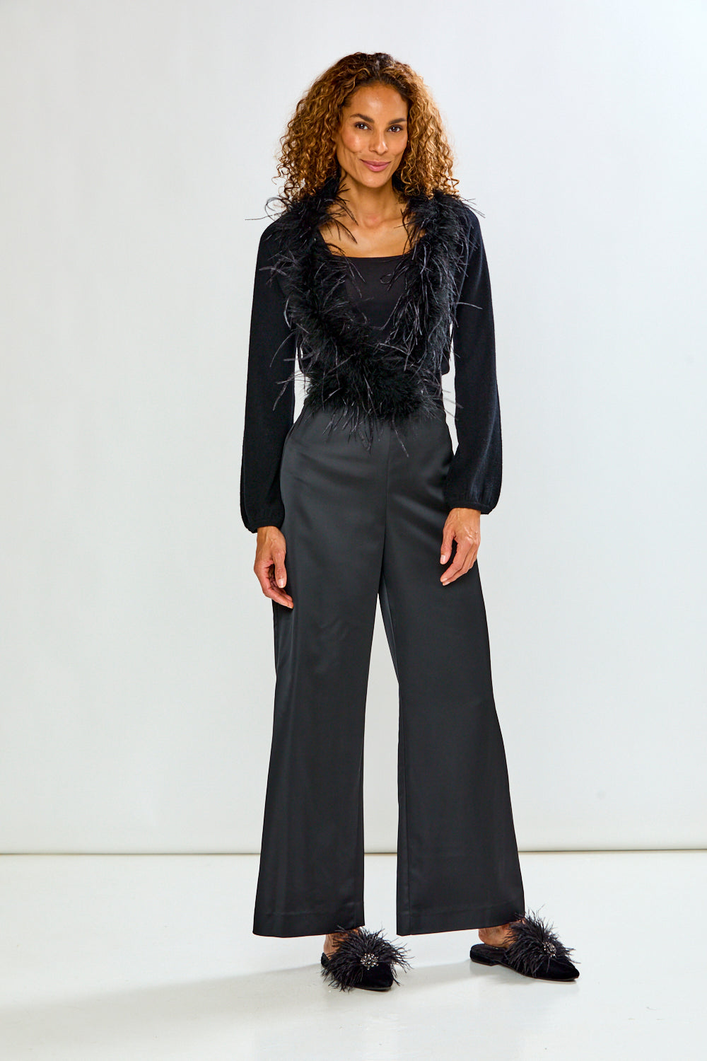 The Reyna Pant - Black shown as black wide leg women's pants styled with a sheer black blouse and feathered shoes in a chic studio look
