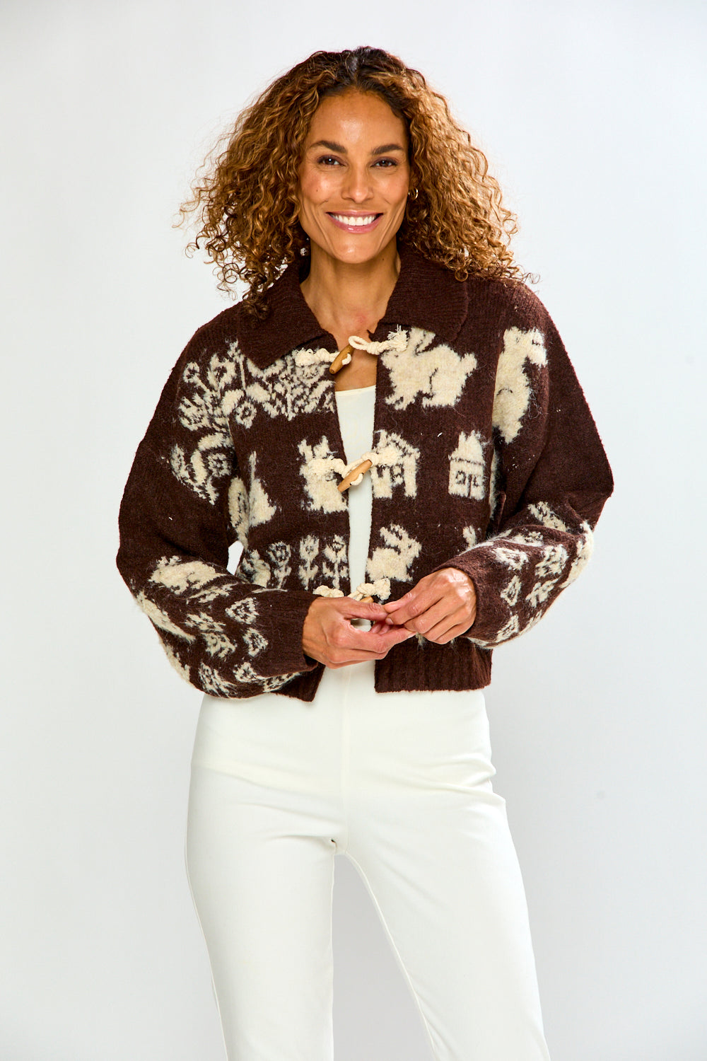 The Bunny Toggle Sweater - Brown Multi worn by a smiling model featuring a brown and cream bunny pattern and wooden toggle closures