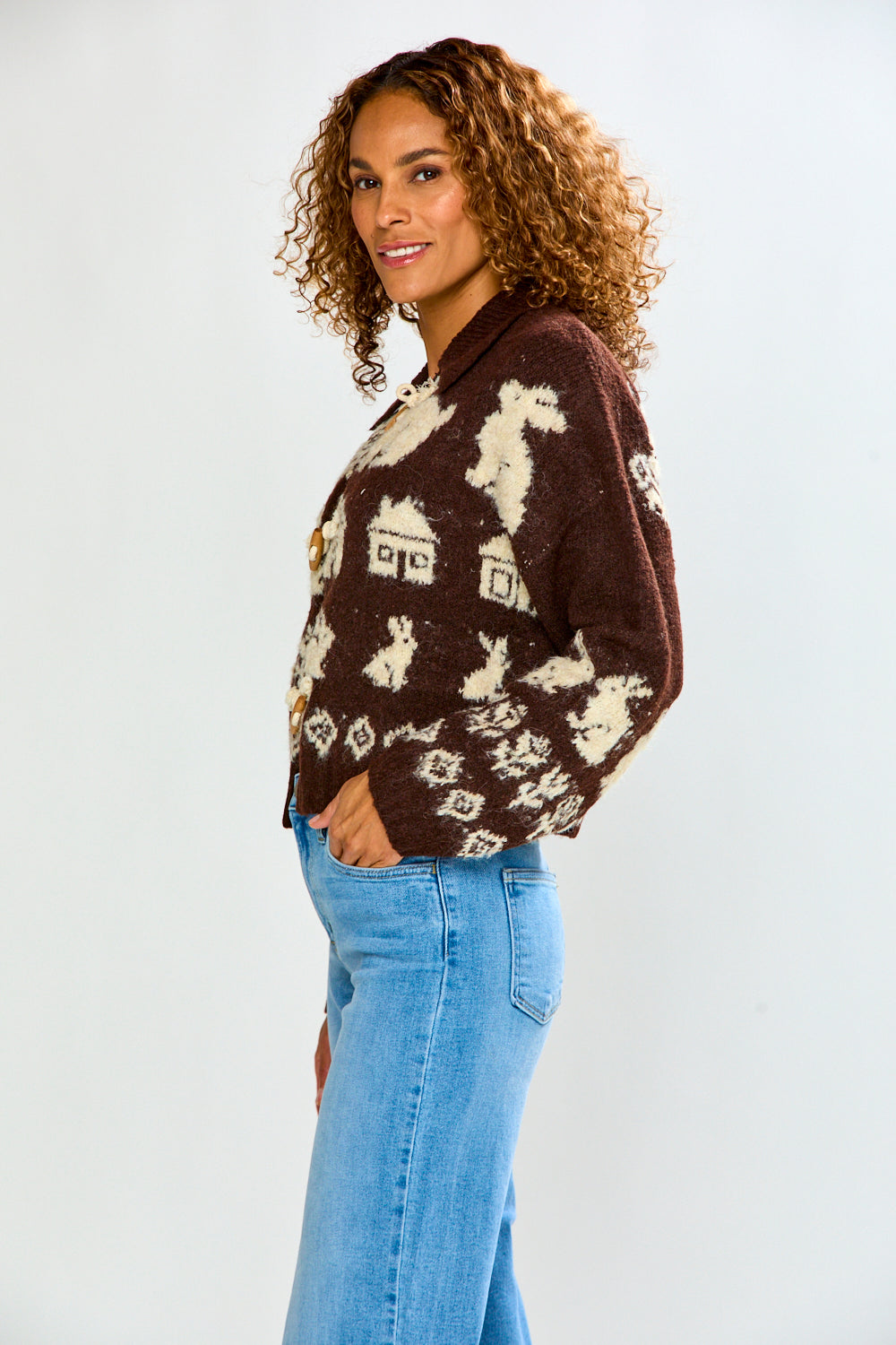 Woman modeling The Bunny Toggle Sweater - Brown Multi, a brown knit sweater with cream bunny motifs and toggle closures, paired with blue jeans.