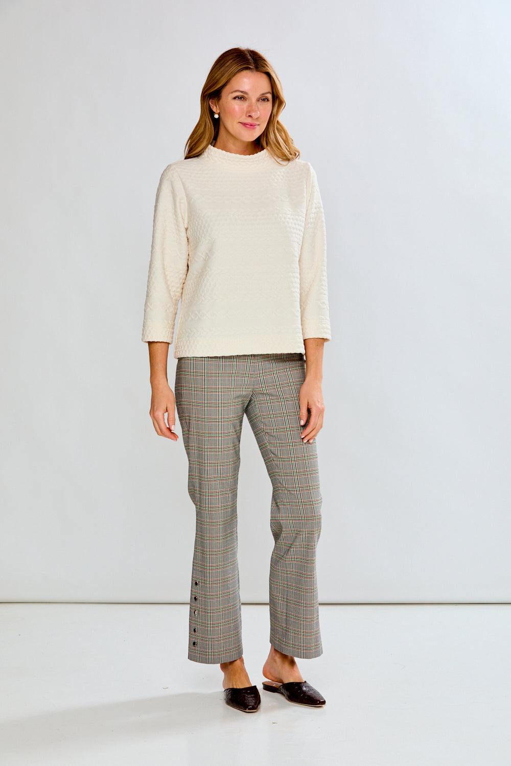 Woman wearing a cream sweater and plaid pants against a white background
