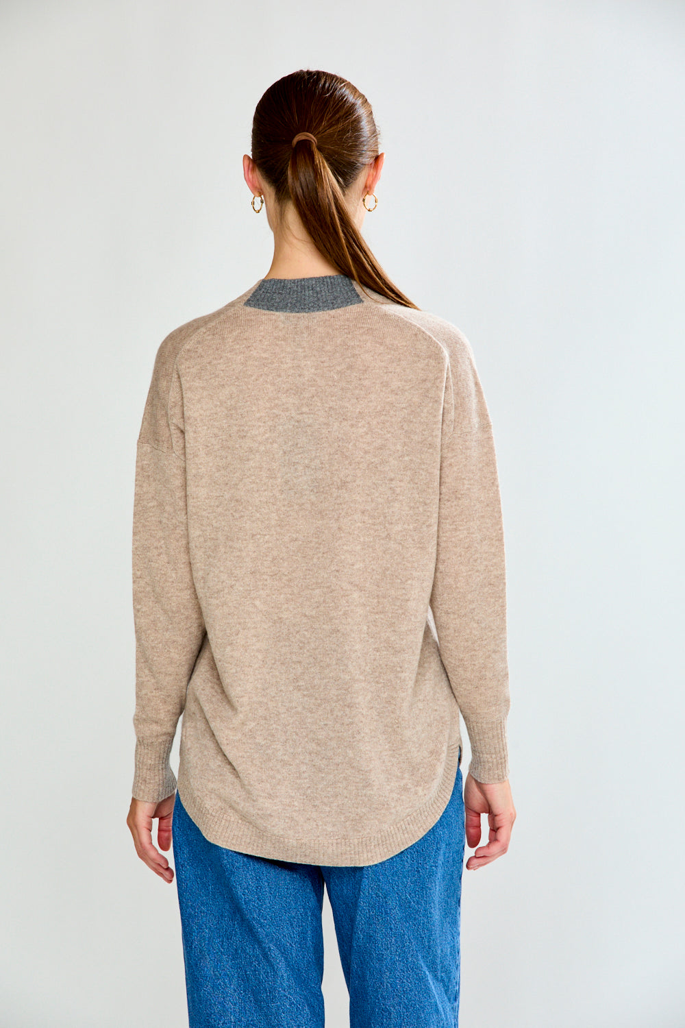 Woman wearing a beige sweater and blue jeans against a white background