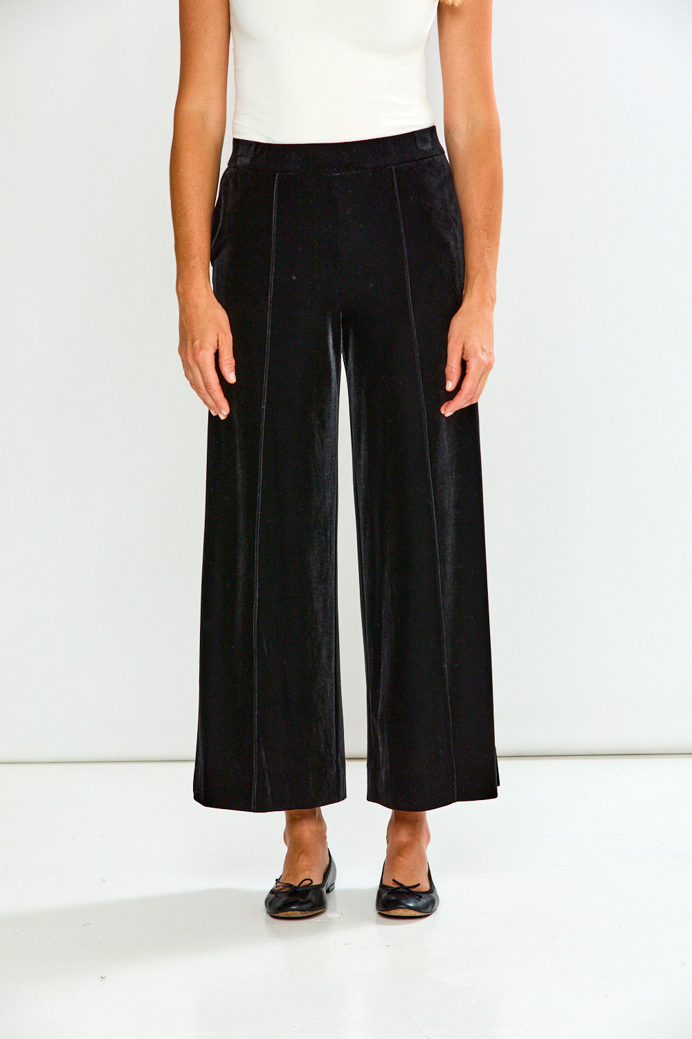 Person wearing black wide-leg pants and a white top on a white background